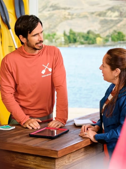 Business owner consulting with a customer at a kayak rental shop by a lake