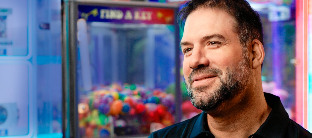 Smiling business owner inside his arcade with a claw machine in the background